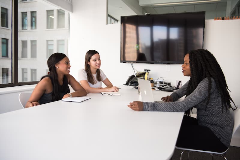 3 women sitting on a white desk and interviewing Feature Image For: Hiring Hacks Your Start-Up Should Be Using Now